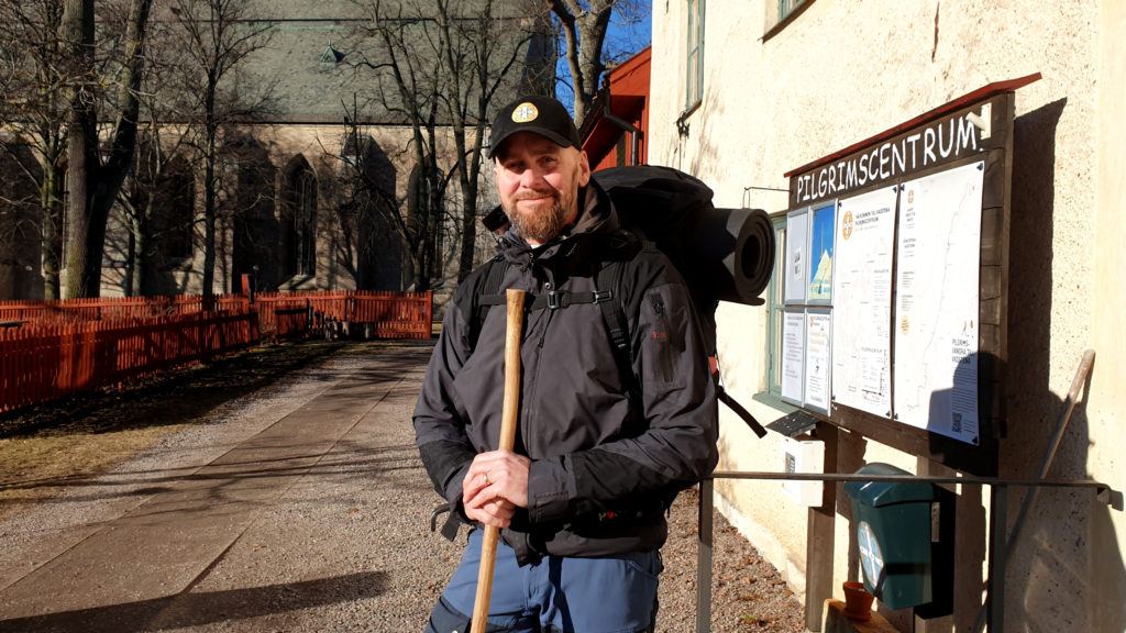 Rickard Borgenback utanför Pilgrimscentrum i Vadstena. Klädd i traditionell pilgrimsoutfit med staven och hatten, ryggsäcken och kängorna. Foto: Björn Andersson.